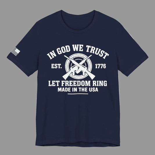 Navy Blue unisex t-shirt with white “IN GOD WE TRUST” crossed-rifles graphic and “LET FREEDOM RING” text, left-sleeve flag graphic, grey background.