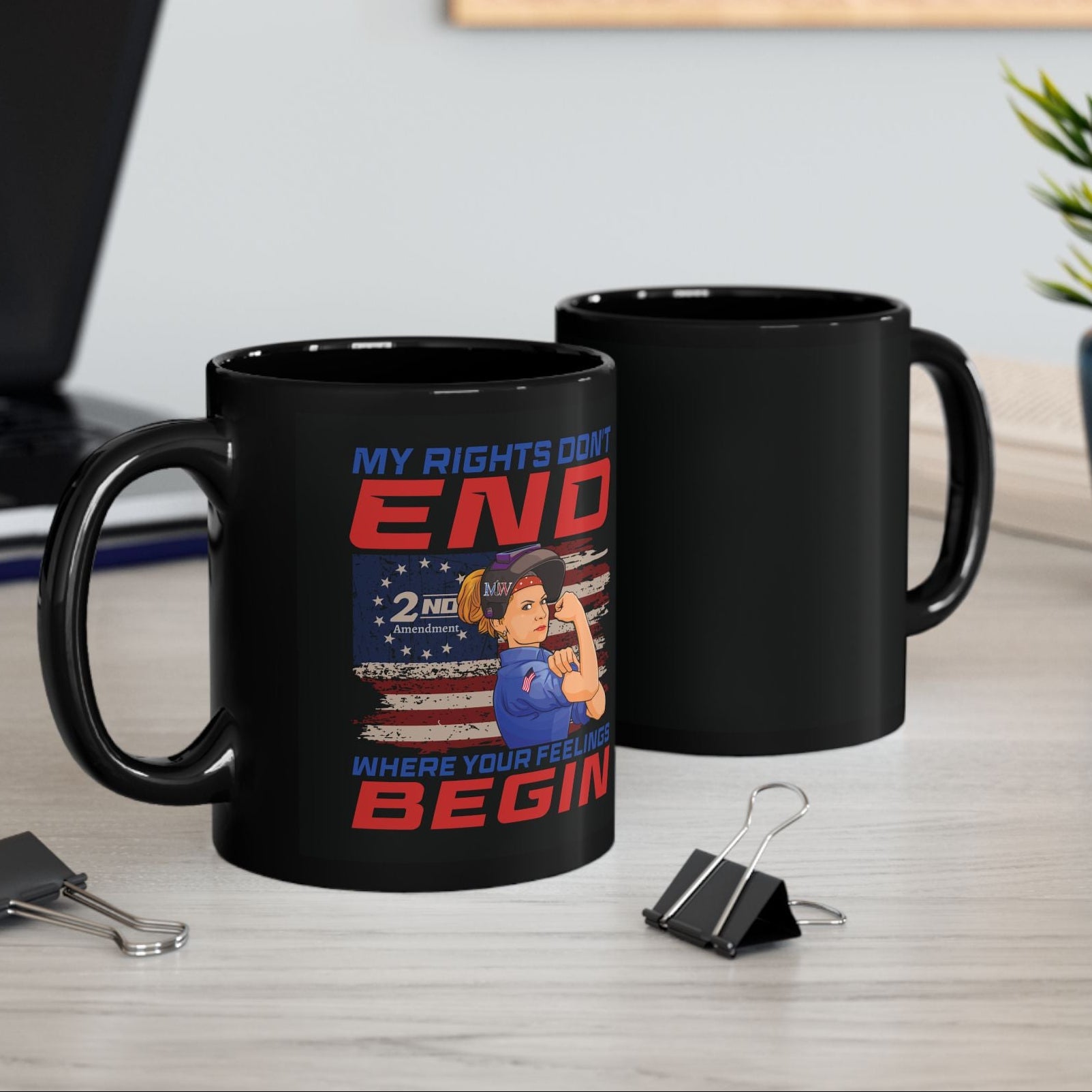 wo black ceramic mugs on a desk—one showing the “MY RIGHTS DON’T END WHERE YOUR FEELINGS BEGIN” 2A design—next to office clips and a small plant.