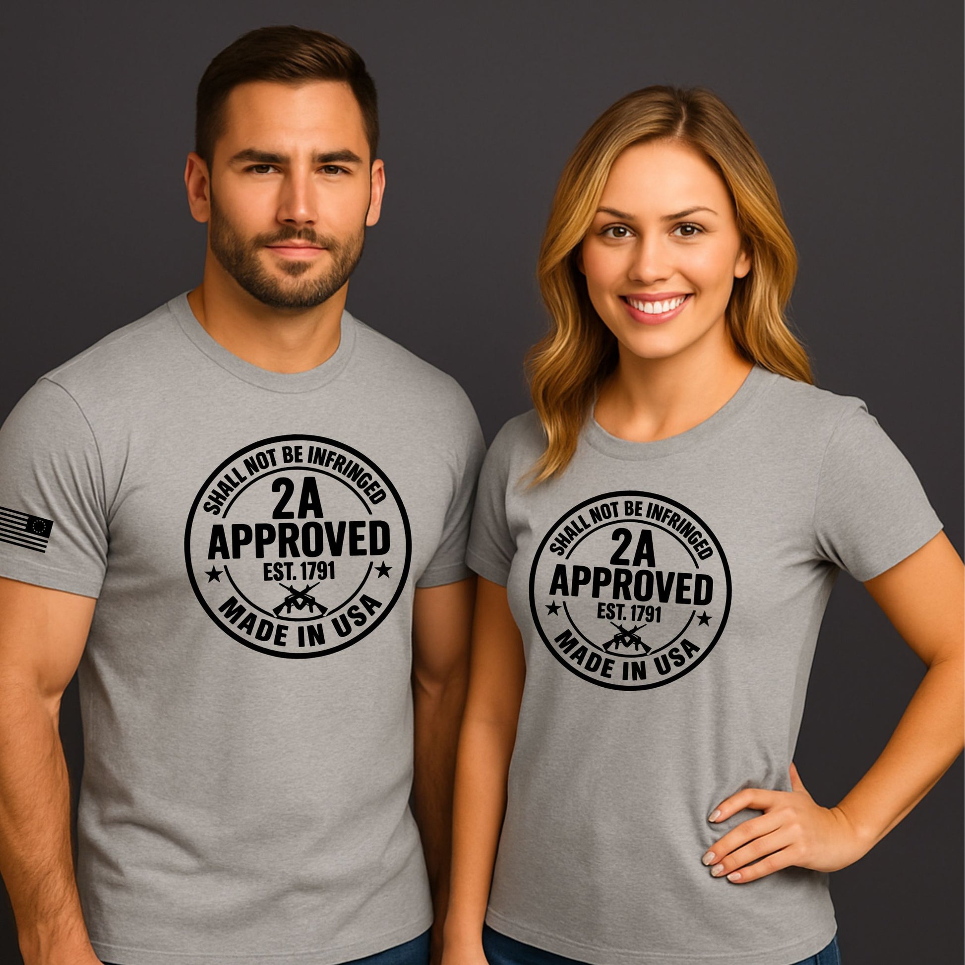 Man and woman wearing light gray ‘2A Approved – Shall Not Be Infringed’ t-shirts with circular logo and American flag sleeve on a dark background.