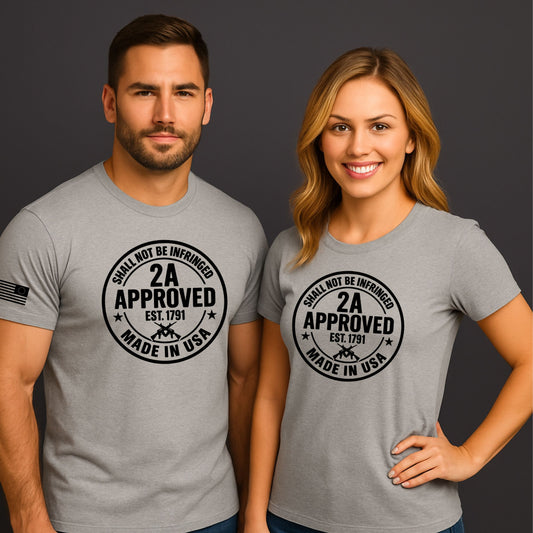 Man and woman wearing light gray ‘2A Approved – Shall Not Be Infringed’ t-shirts with circular logo and American flag sleeve on a dark background.