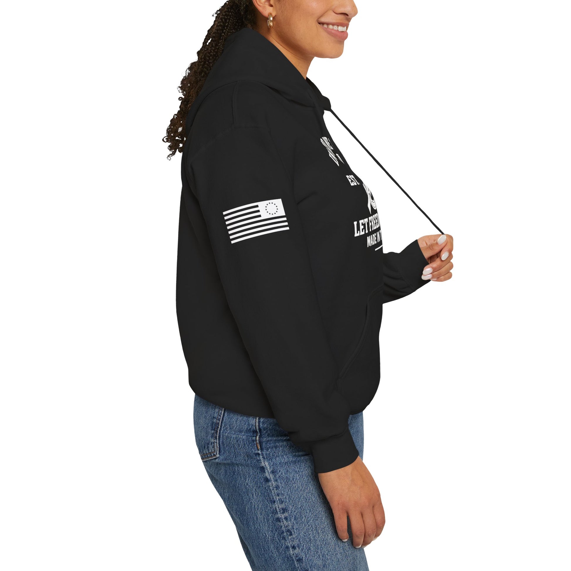 Side view of unisex black hoodie with Betsy Ross flag sleeve detail and “In God We Trust 1776 Let Freedom Ring” graphic, mockup