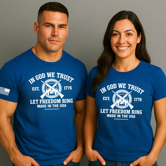 Unisex royal blue t-shirt, white front graphic “IN GOD WE TRUST” with crossed rifles + “LET FREEDOM RING,” gray studio background.