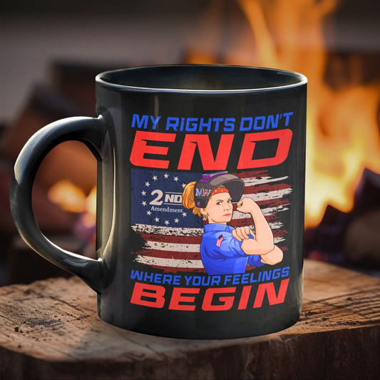 Black ceramic coffee mug with “MY RIGHTS DON’T END WHERE YOUR FEELINGS BEGIN” design and Rosie-style welder graphic, on a wooden surface with firelight in the background.