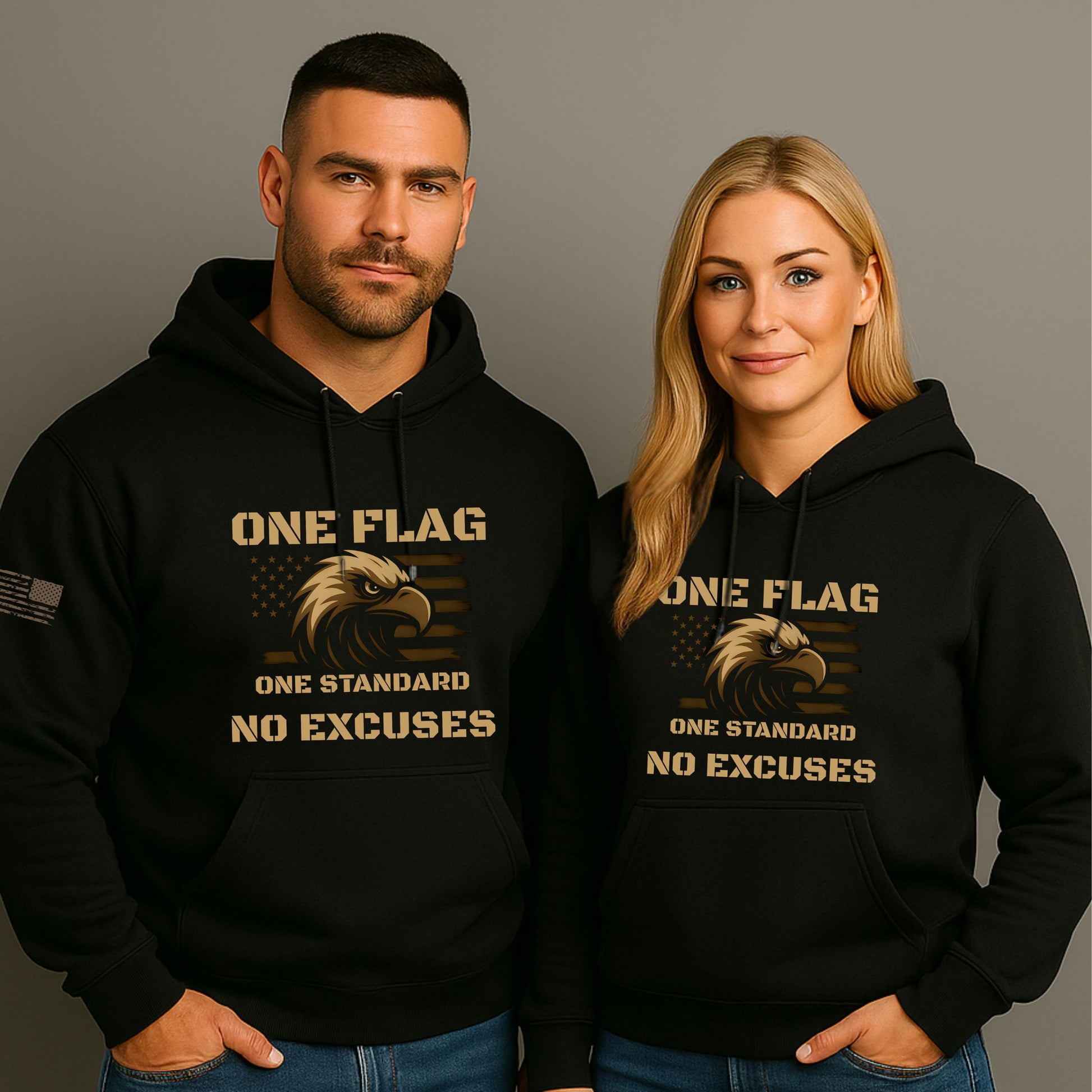 Man and woman wearing black ‘One Flag One Standard No Excuses’ hoodies with bronze eagle and American flag graphic, on a gray studio background.